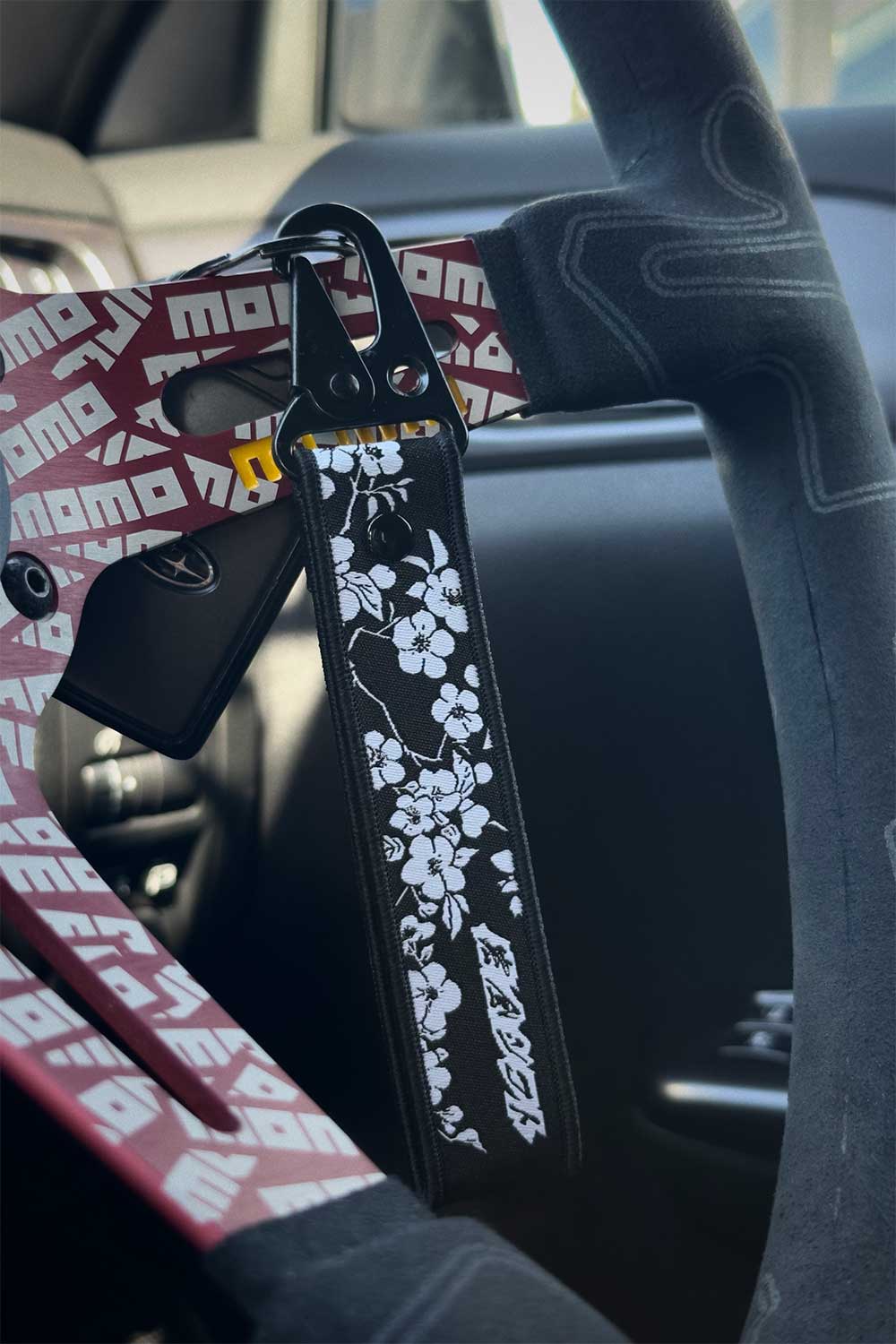 A hand holding a JDM great waves lanyard, standing in an open area