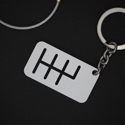 The back of a six-speed manual shift keychain with matte silver finish on a black background