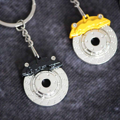 A black brake disc keychain is being focused while a yellow one is placed on the side