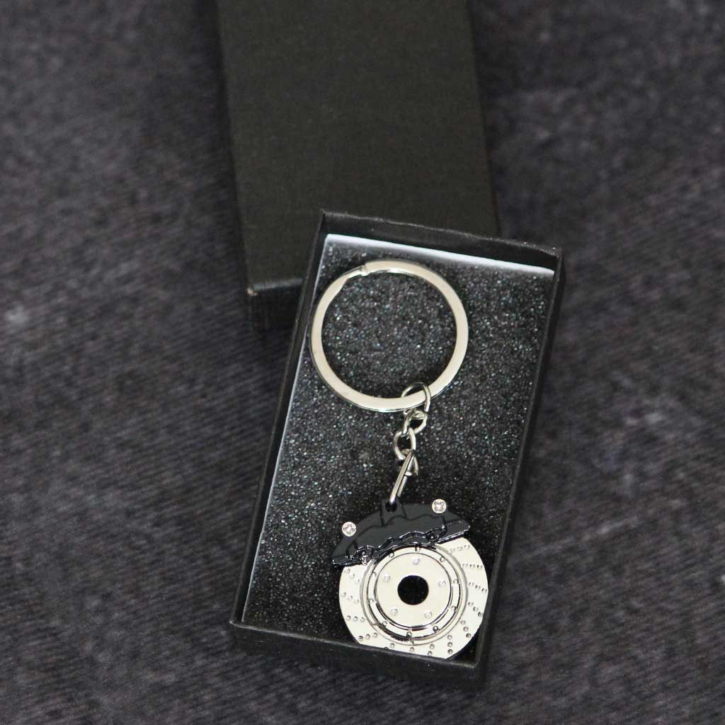 A black brake disc keychain in a gift box on a dark grey background