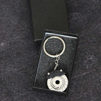 A black brake disc keychain in a gift box on a dark grey background