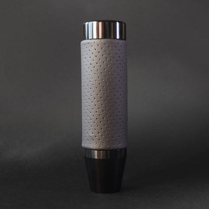 A black leather grip shift knob is standing on a dark grey floor on a dark grey background
