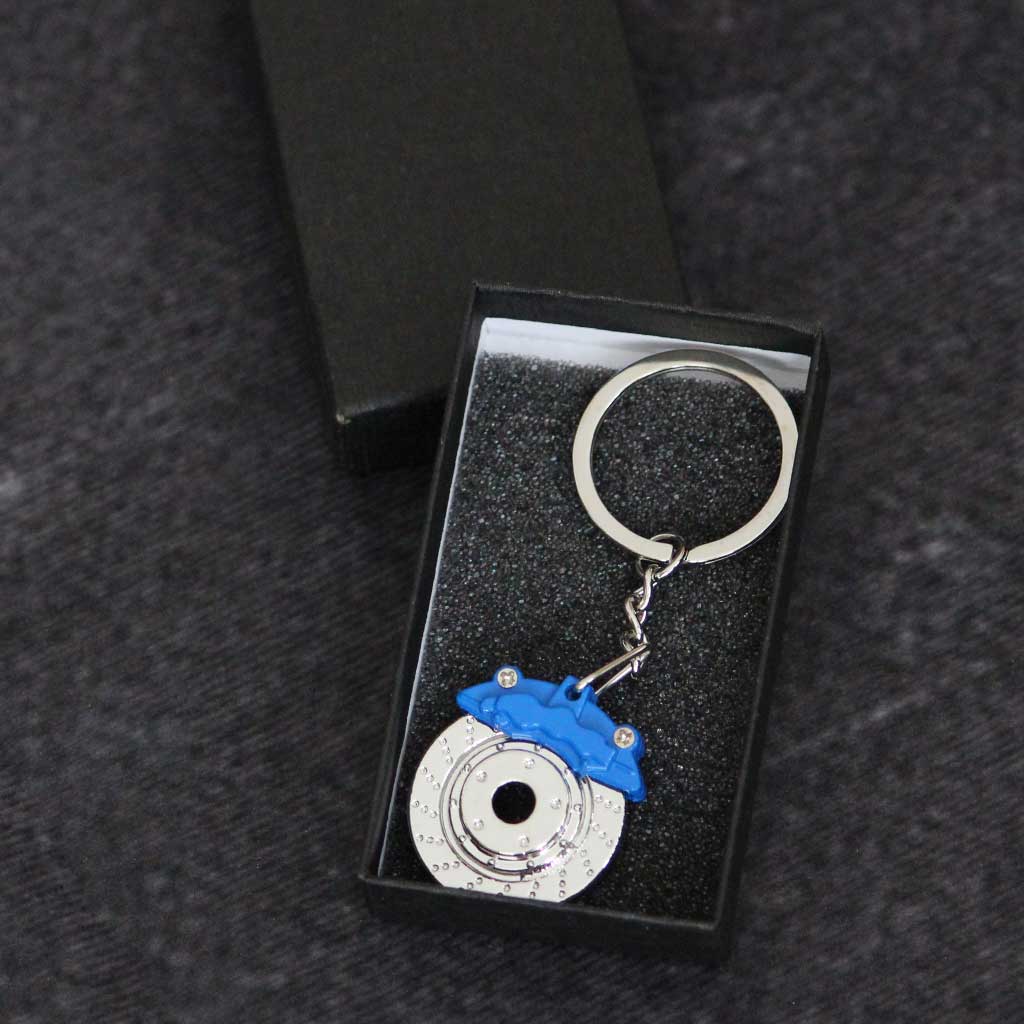 A blue brake disc keychain in a gift box on a dark grey background