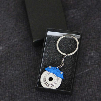 A blue brake disc keychain in a gift box on a dark grey background