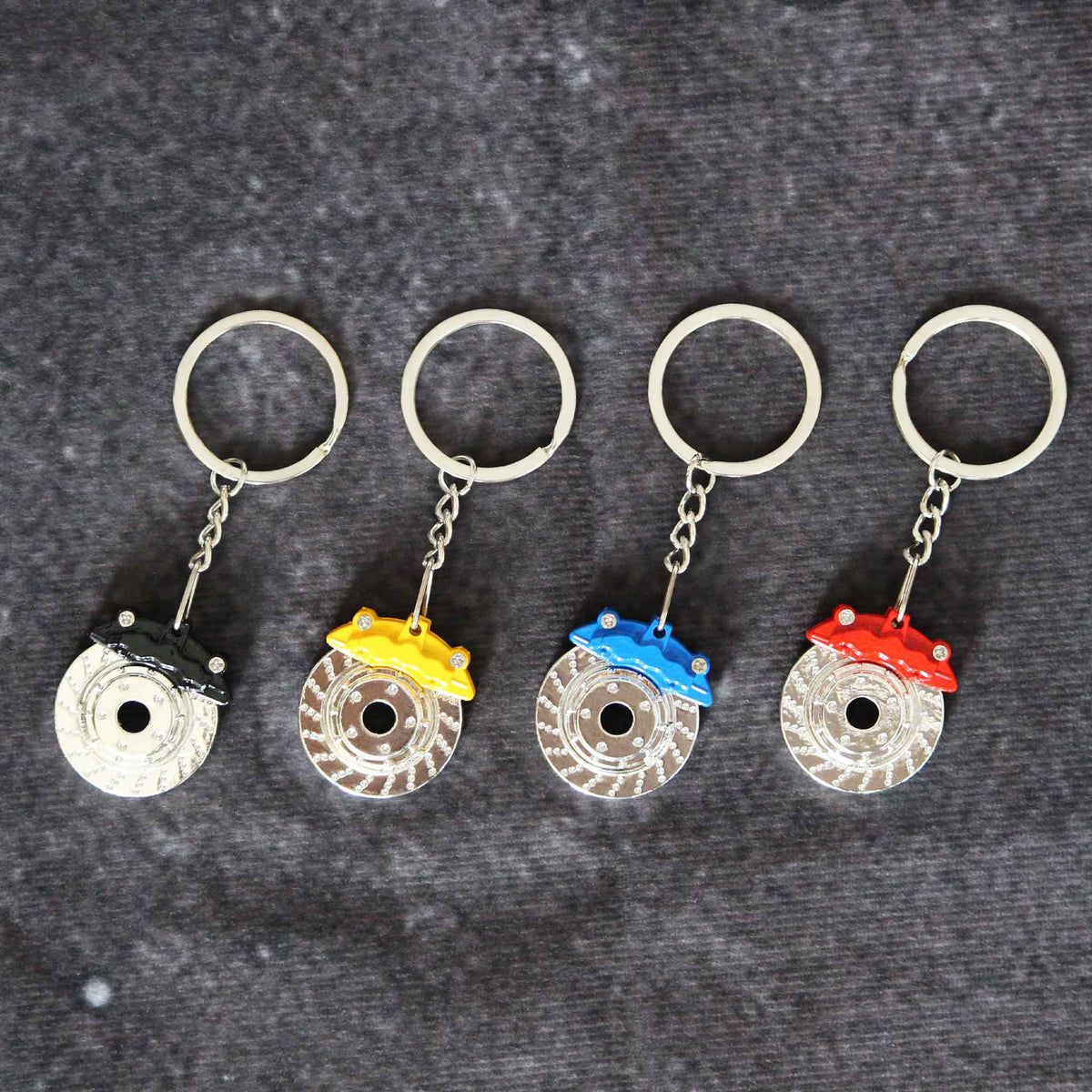Four brake disc with calliper keychains with different colours are placed neatly on a grey background