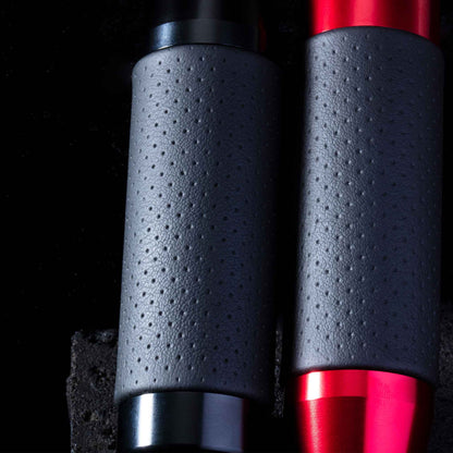 Two leather grip shift knobs are leaning closely towards a black stone on a black background, providing a closer look at the dots on the knobs