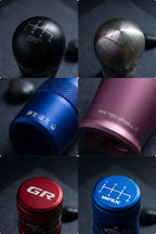 Six close-up product photos arranged in a 3x2 grid showing manual gear shift knobs in different anodized metal colours: black, silver, red, blue, and pink. Each photo is cropped tightly, with customised laser engravings visible on the metal surfaces, including STI, Fairlady Z, GR, WRX, and difference H-patterns.
