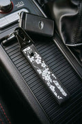 A black embroidered car keychain strap with white sakura cherry blossom silhouettes, attached to a Subaru STI key ring and placed on a car center console.