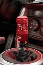 A red manual gear shift knob with white etched koi fish designs and a Perfect Shift logo, set inside a Toyota 86's center console.