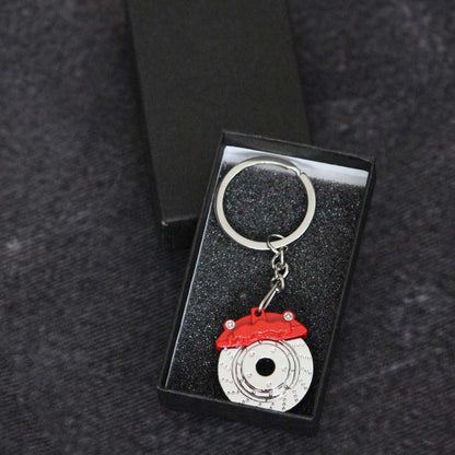 A red brake disc keychain in a gift box on a dark grey background