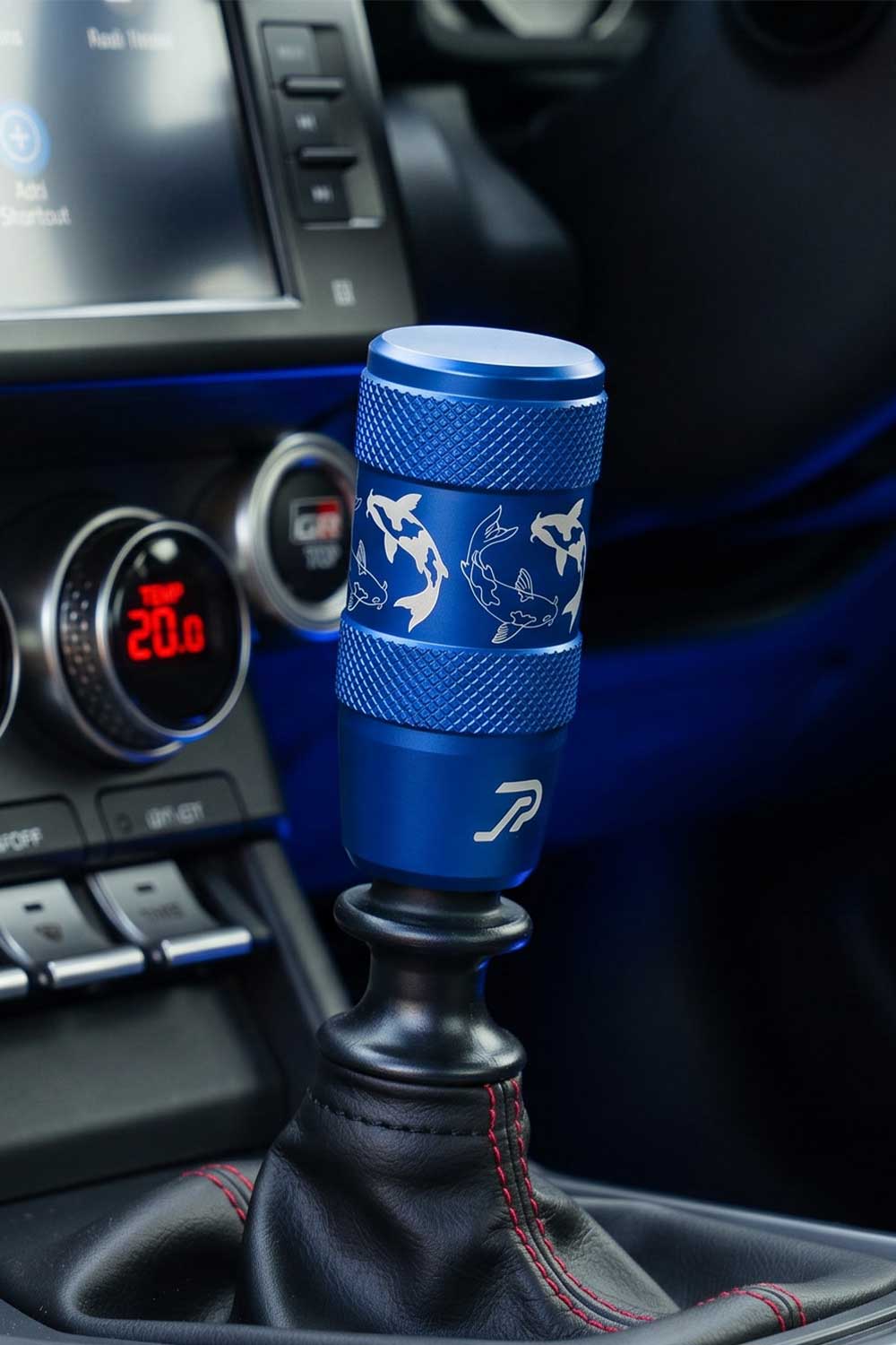A blue anodized aluminum manual gear shift knob with white fish graphics and a Perfect Shift logo, installed in a Toyota GR86's center console.