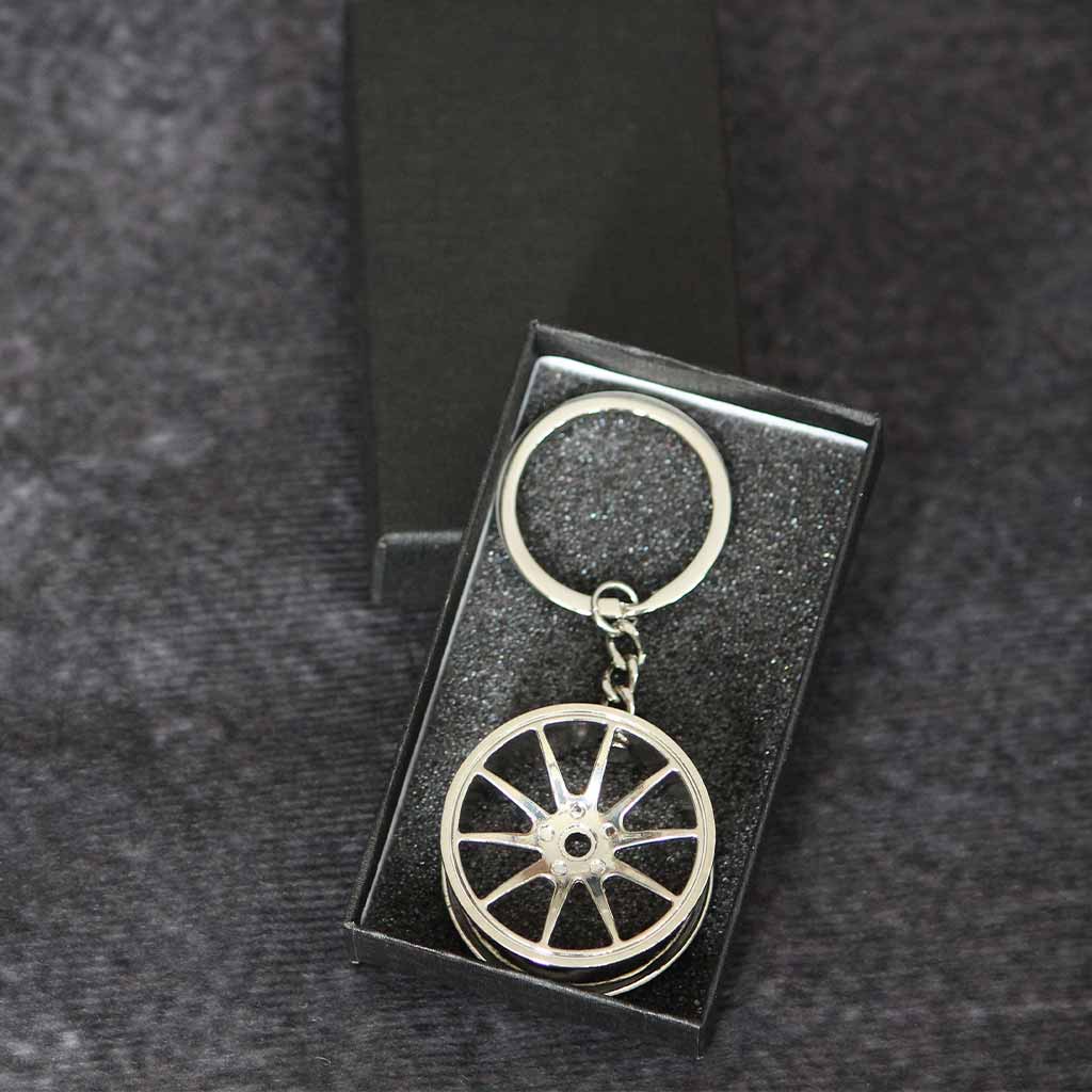 A silver wheel keychain in a black gift box on a dark grey background