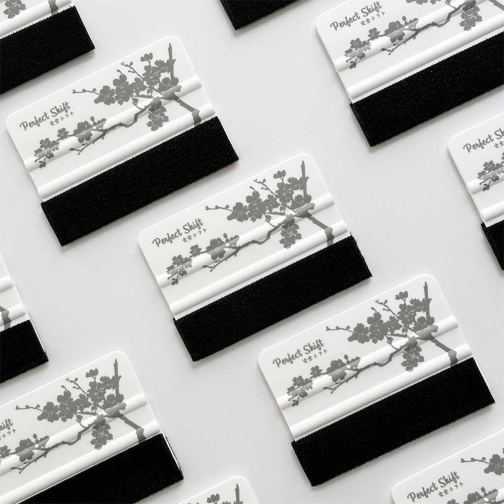 Several JDM banner sticker application squeegees with cherry blossom pattern and Perfect Shift logo orderly placed on a white background