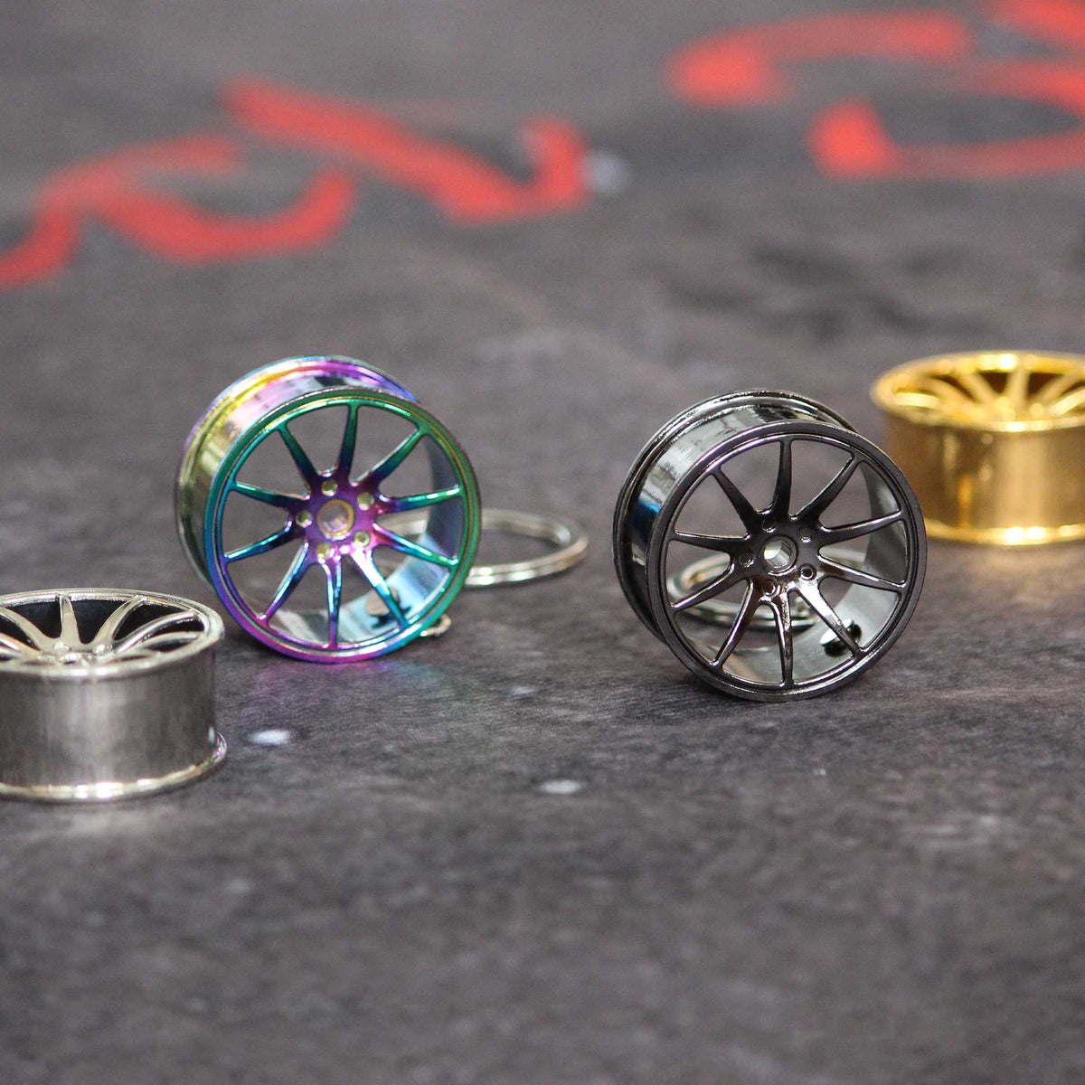 Four wheel keychains placed on a grey floor, two are standing, the other two are laying