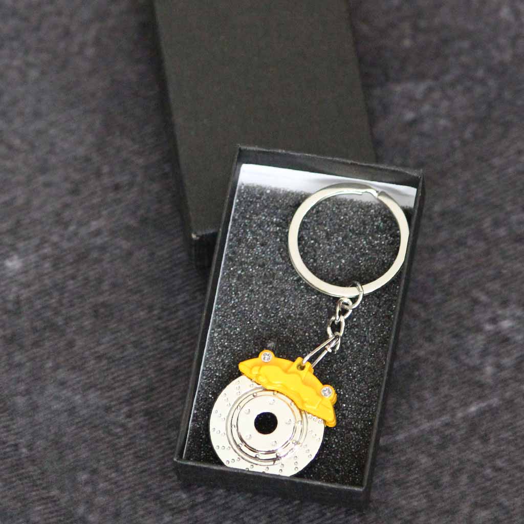 A yellow brake disc keychain in a gift box on a dark grey background